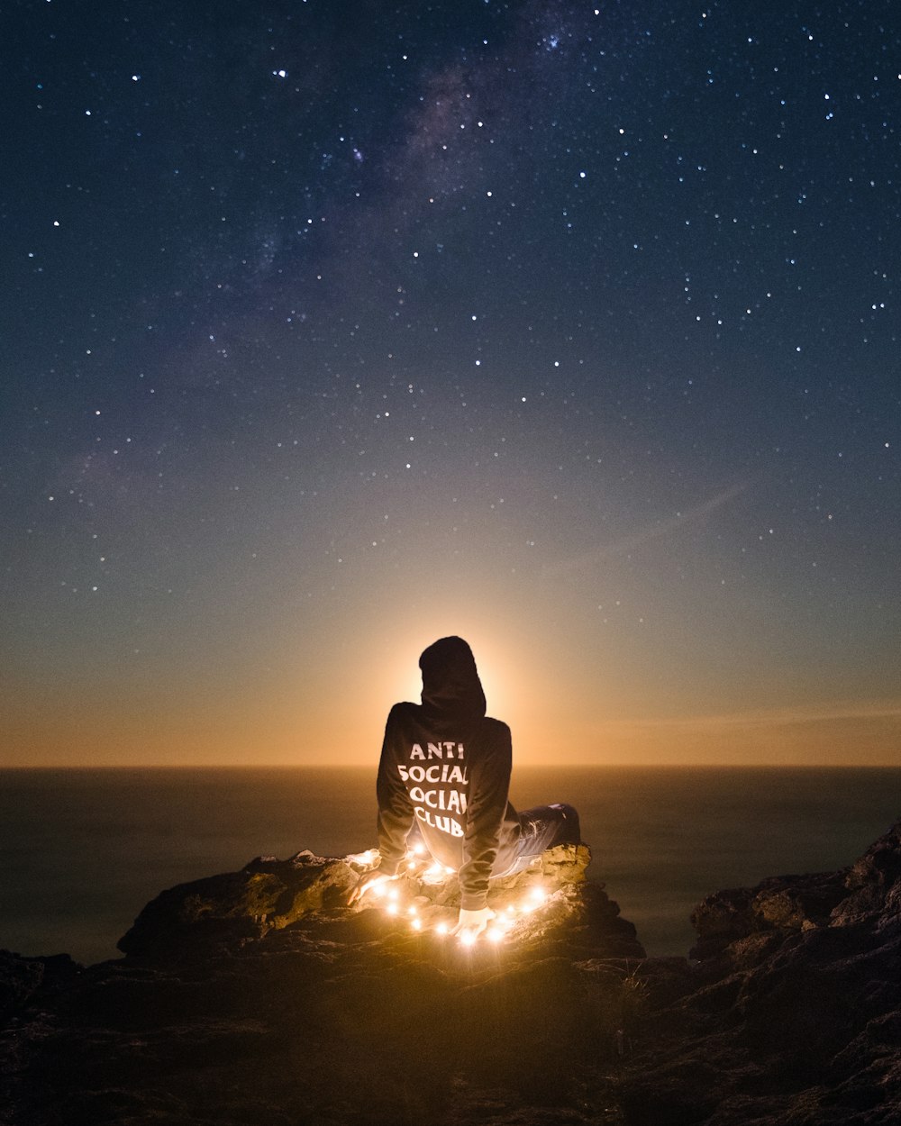 person wearing black anti social social club hoodie sitting on mountain cliff