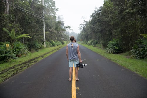 Man in the middle of a road holding a DSLR camera for recording a TikTok video.