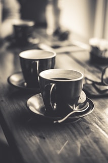 A cozy picture of two coffee cups side by side on a wooden table.