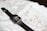 A smartwatch with a black band is resting on an unfolded map. The smartwatch screen displays a cartoon character pointing at the clock hands.