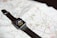A smartwatch with a black band is resting on an unfolded map. The smartwatch screen displays a cartoon character pointing at the clock hands.