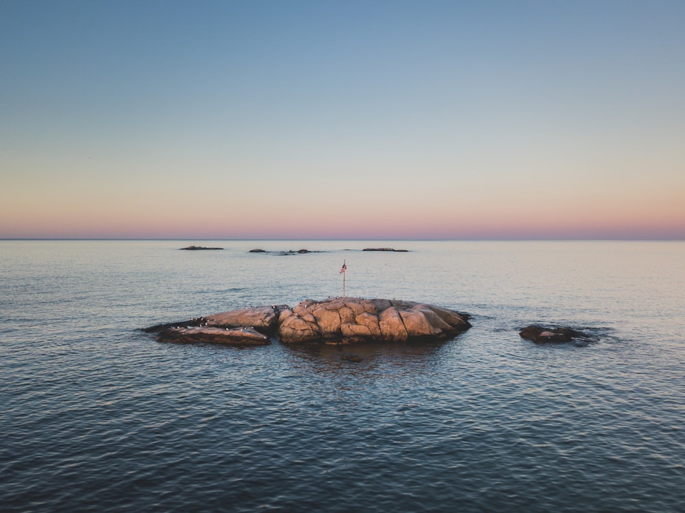 landscape photography of red flag on rock in the middle on ocean
