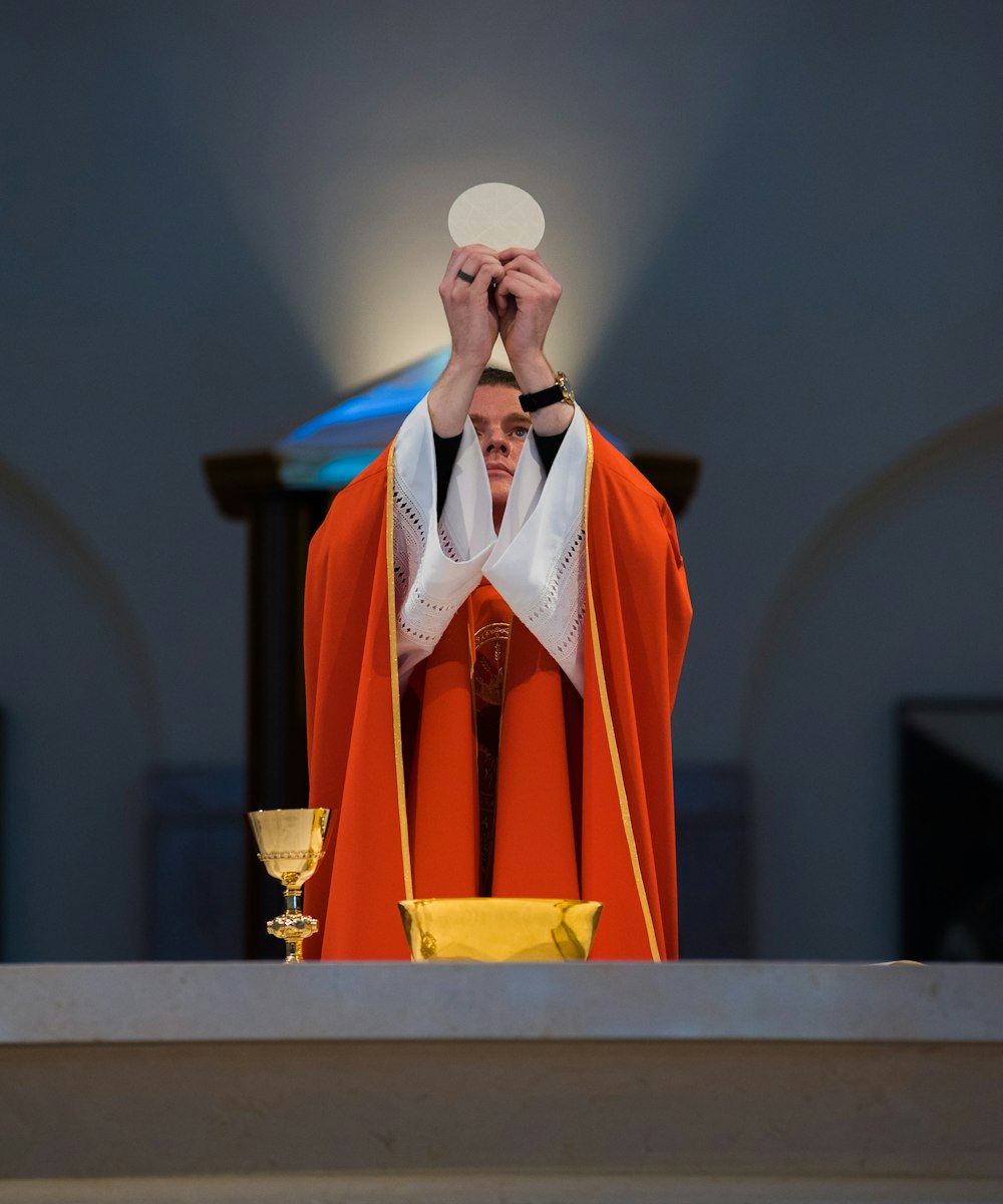 Um sacerdote com um manto vermelho oferecendo comunhão em frente a um altar em Kingwood