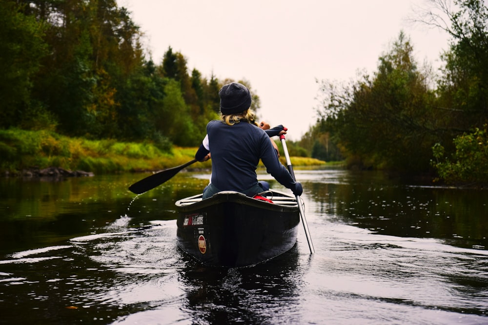 Persona in camicia blu a maniche lunghe che si siede sul kayak mentre pagaia sullo specchio d'acqua durante il giorno