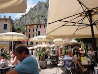 A bustling café terrace filled with people engaged in animated conversations under colorful umbrellas.