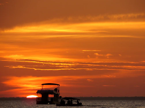 A vibrant sunset over calm waters with a charter boat silhouetted against the colorful sky.