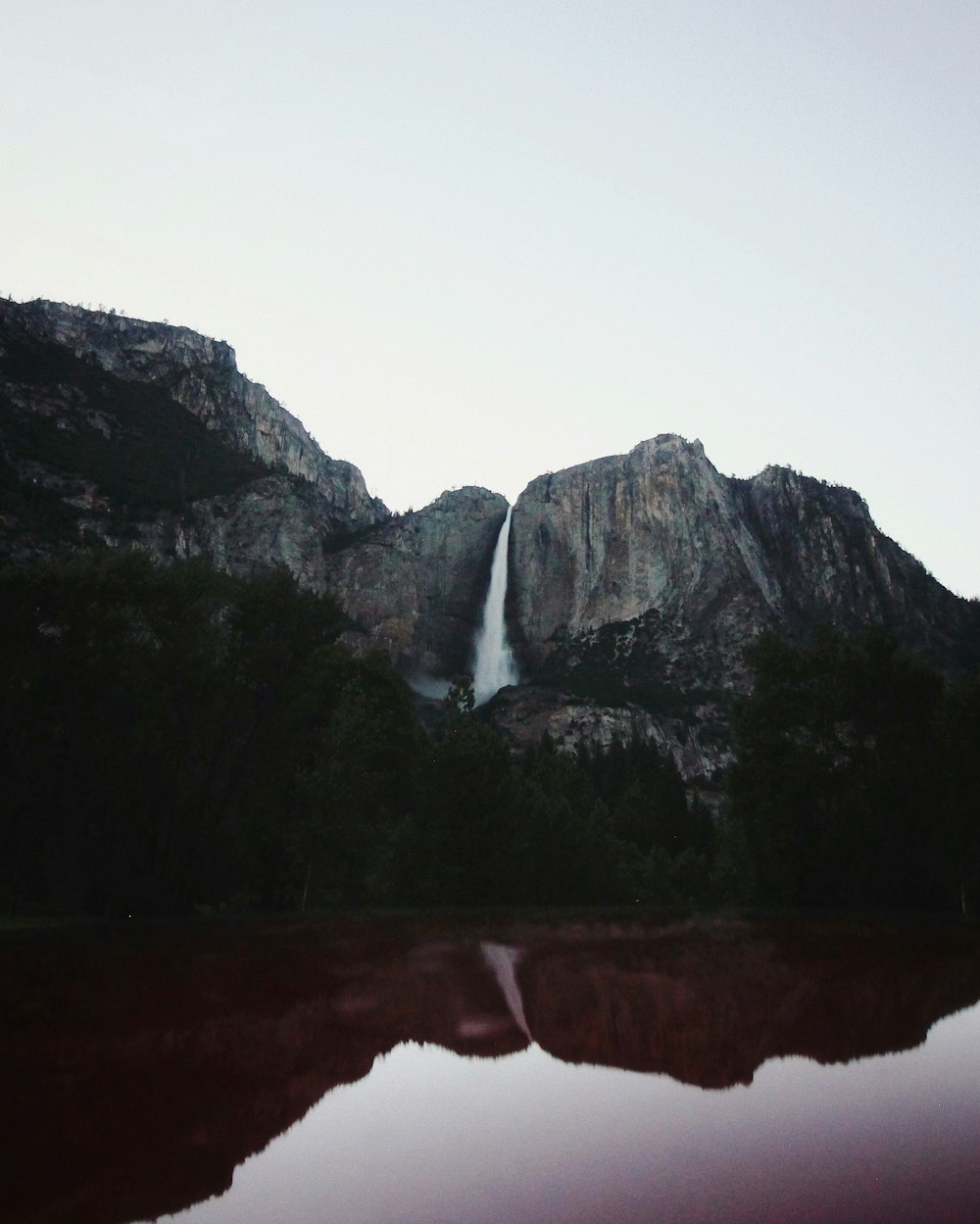 A narrow waterfall going down a drop off a rocky mountain.