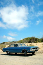 A vintage car parked beside a rustic roadside café under a clear blue sky.