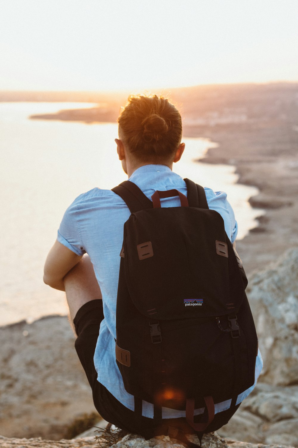 person in black knapsack sitting on cliff