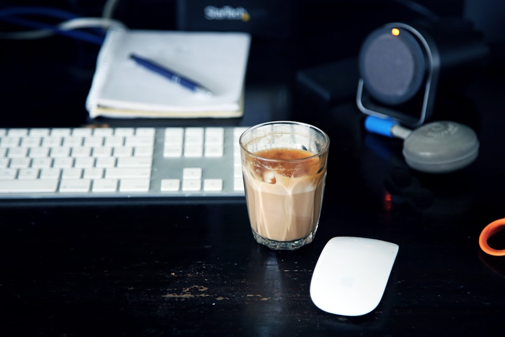 clear glass shot glass beside Apple Magic Mouse