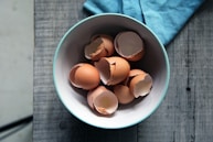 brown eggshells in round white ceramic bowl on gray wooden board top-view photography