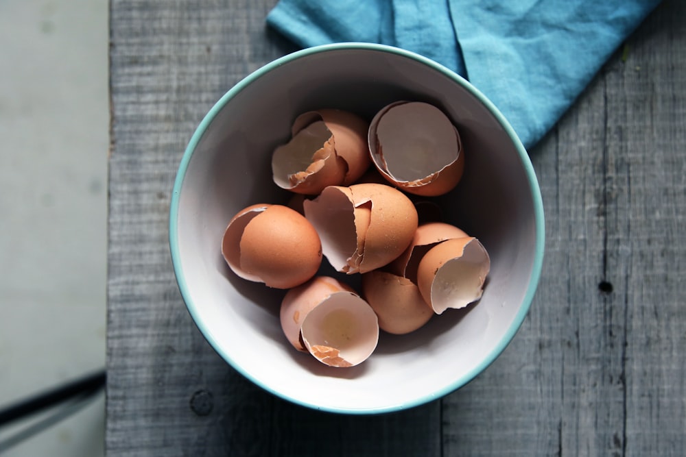 brown eggshells in round white ceramic bowl on gray wooden board top-view photography