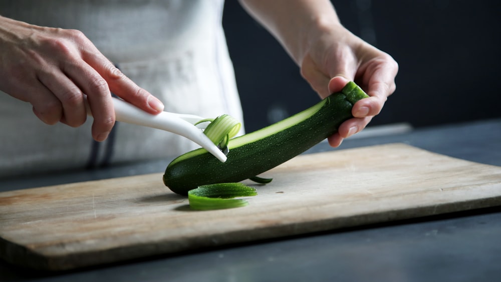 person pealing green cucumber inside room