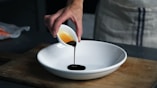 person dripping black liquid from small white ceramic bowl to big white ceramic bowl