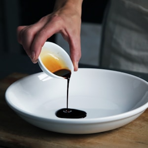 person dripping black liquid from small white ceramic bowl to big white ceramic bowl