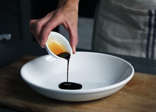 person dripping black liquid from small white ceramic bowl to big white ceramic bowl