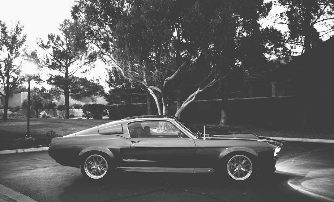 grayscale photo of coupe parked near trees