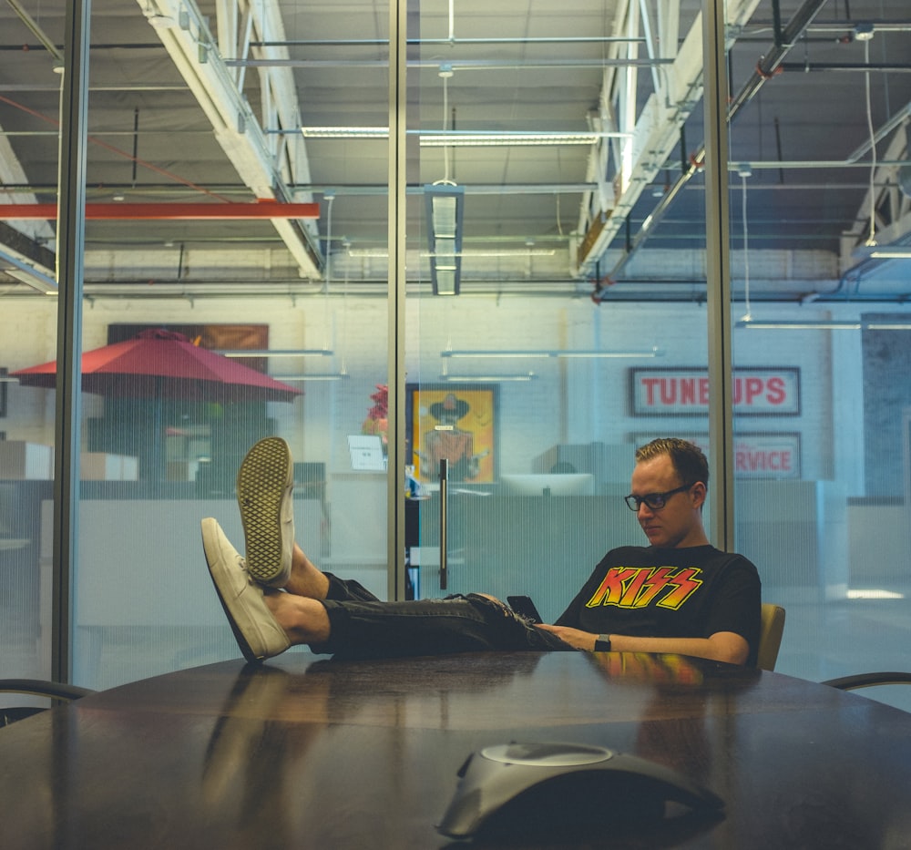 man sitting beside table wearing black kiss-printed T-shirt