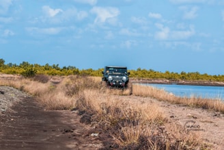 A rugged Range Rover driving over a gravel path beside the ocean.