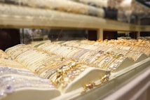 A display case filled with various pieces of gold and silver jewelry, including bracelets and necklaces, arranged in an organized fashion under bright lighting.