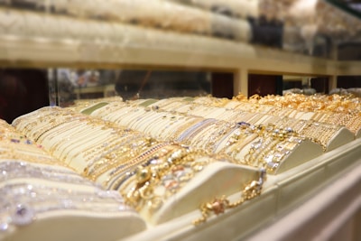 A display case filled with various pieces of gold and silver jewelry, including bracelets and necklaces, arranged in an organized fashion under bright lighting.