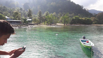 A cheerful traveler booking a scenic boat tour on a mobile device near a Caribbean beach.