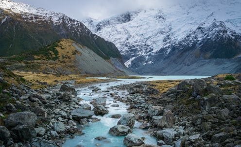 river with gray rocks near mountain covered in snow