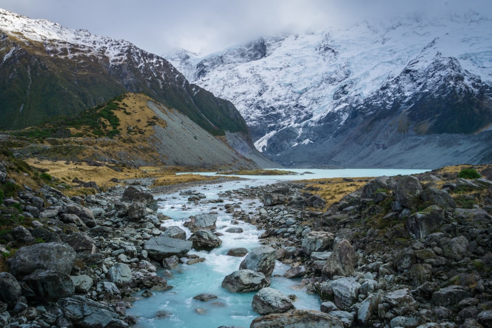 river with gray rocks near mountain covered in snow