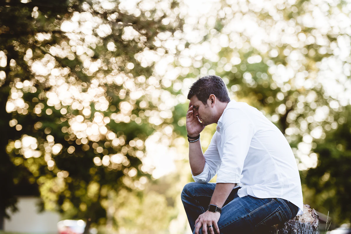 Worried man sitting outdoors with his head resting on his hand, illustrating how chronic stress can contribute to erectile dysfunction.