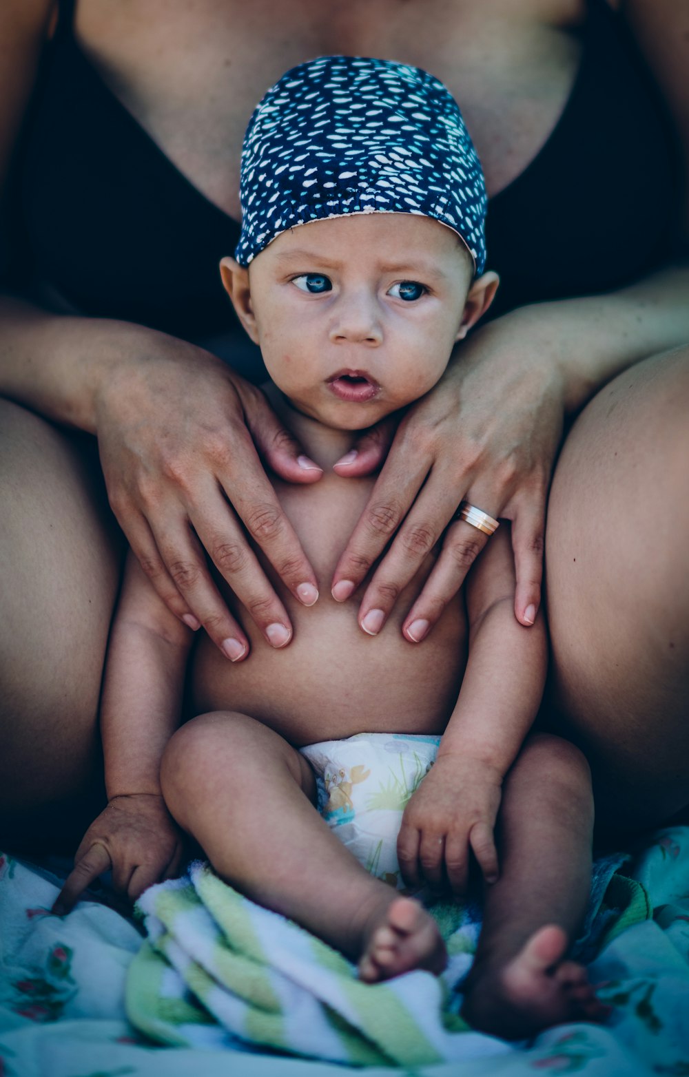 baby wearing white and black cap near woman wearing black bra