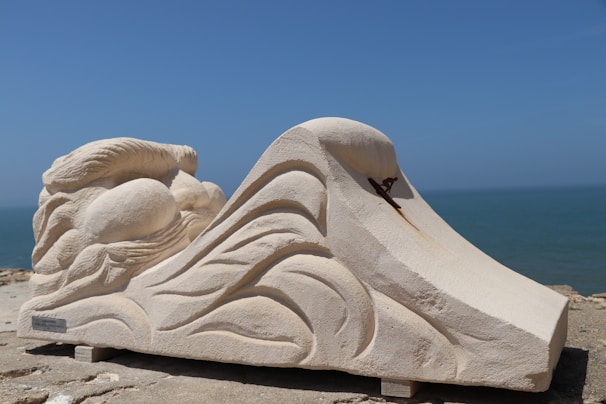 Custom-made cement sculpture inspired by ocean waves, displayed on a sandy surface.