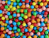 A collection of brightly colored gumballs in various hues including yellow, red, blue, green, orange, and pink, densely packed together.