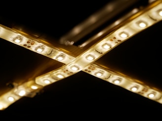 Two LED light strips arranged in a crisscross pattern against a dark background. The strips emit a warm yellowish glow and show detailed circuitry and components.