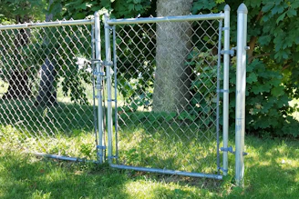 A robust chain link gate securing a spacious farm entrance surrounded by green fields.