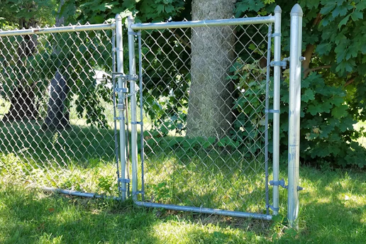 A robust chain link gate securing a spacious farm entrance surrounded by green fields.