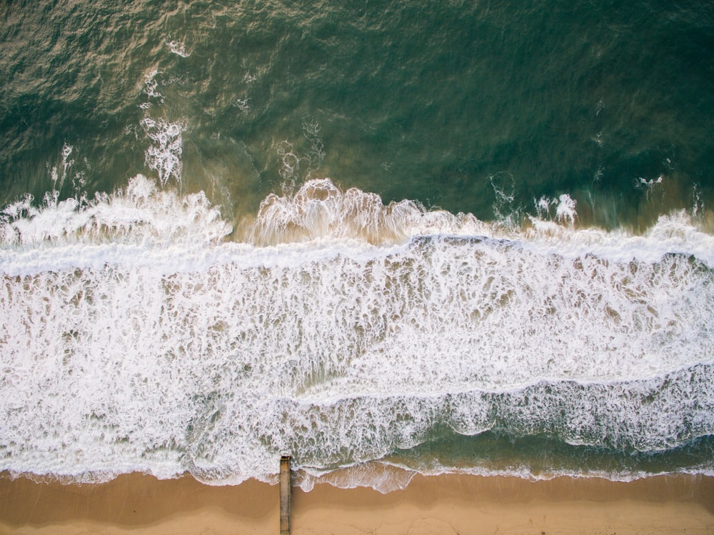 Fotografía de la vista superior de la arena marrón de la playa con el agua verde azulada del océano durante el día