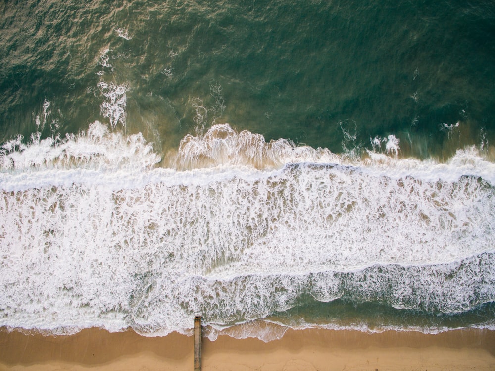 Fotografia de vista superior da areia marrom da praia com água do oceano durante o dia