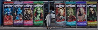 Large colorful posters of movie characters lined up at a bus stop advertising a film titled 'Guardians of the Galaxy Vol. 2'. A woman is seen walking in front of the posters.
