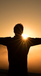 silhouette photo of man on cliff during sunset