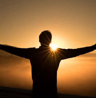 silhouette photo of man on cliff during sunset