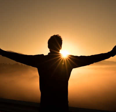 silhouette photo of man on cliff during sunset