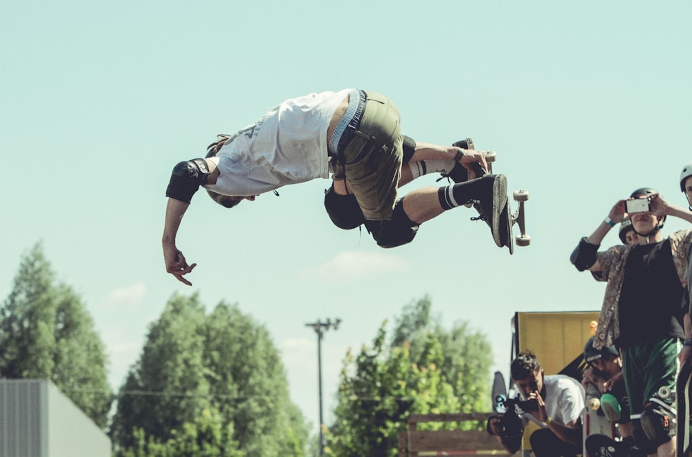 uomo che tiene lo skateboard mentre fa acrobazie durante il giorno