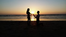 A sunset silhouette of the couple holding hands on a beach.