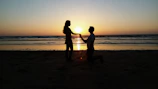 A sunset silhouette of a couple holding hands on a quiet beach.