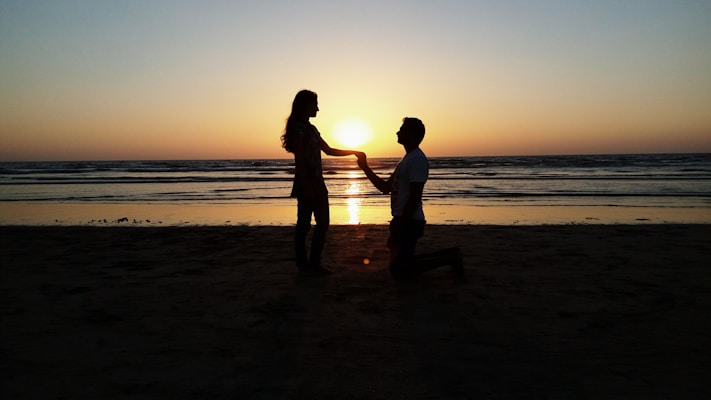 A sunset silhouette of the couple holding hands on a beach.