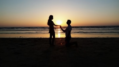 Sunset silhouette of a couple holding hands on a beach with waves gently rolling in.