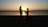A romantic silhouette of a couple holding hands at sunset on a beach.