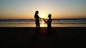 A sunset silhouette of a couple holding hands on a quiet beach.