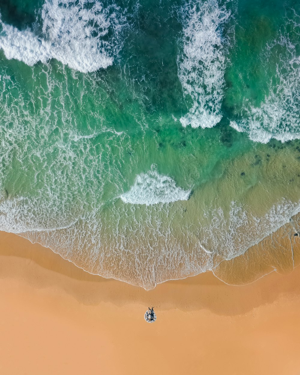 Fotografia con vista dall'alto di sabbia marrone sulla spiaggia con acqua verde acqua dell'oceano durante il giorno
