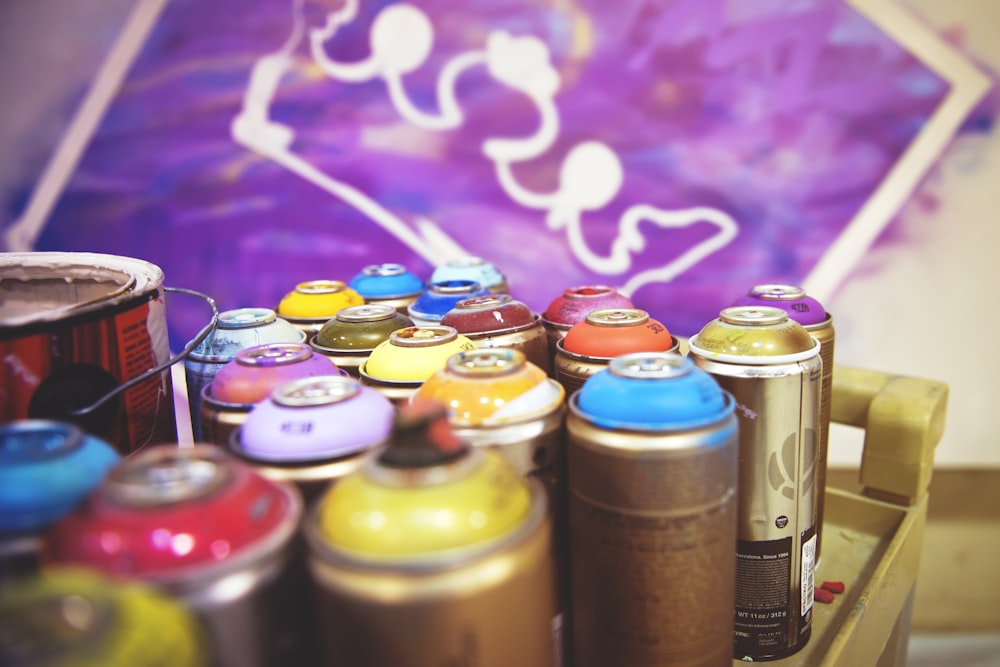 closeup photography of assorted-color paint spray cans beside purple and white crown painting